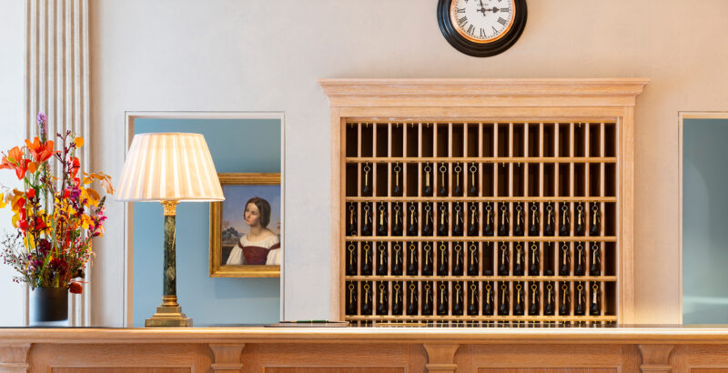 Klassische Hotelrezeption mit hölzernem Schlüsselfach und frischem Blumenarrangement.