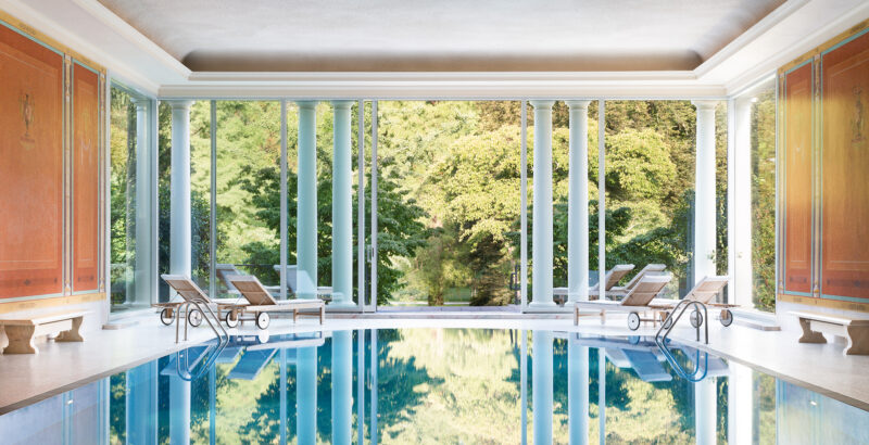 Großer Indoor-Pool mit bodentiefen Fenstern und Blick auf die Parklandschaft.