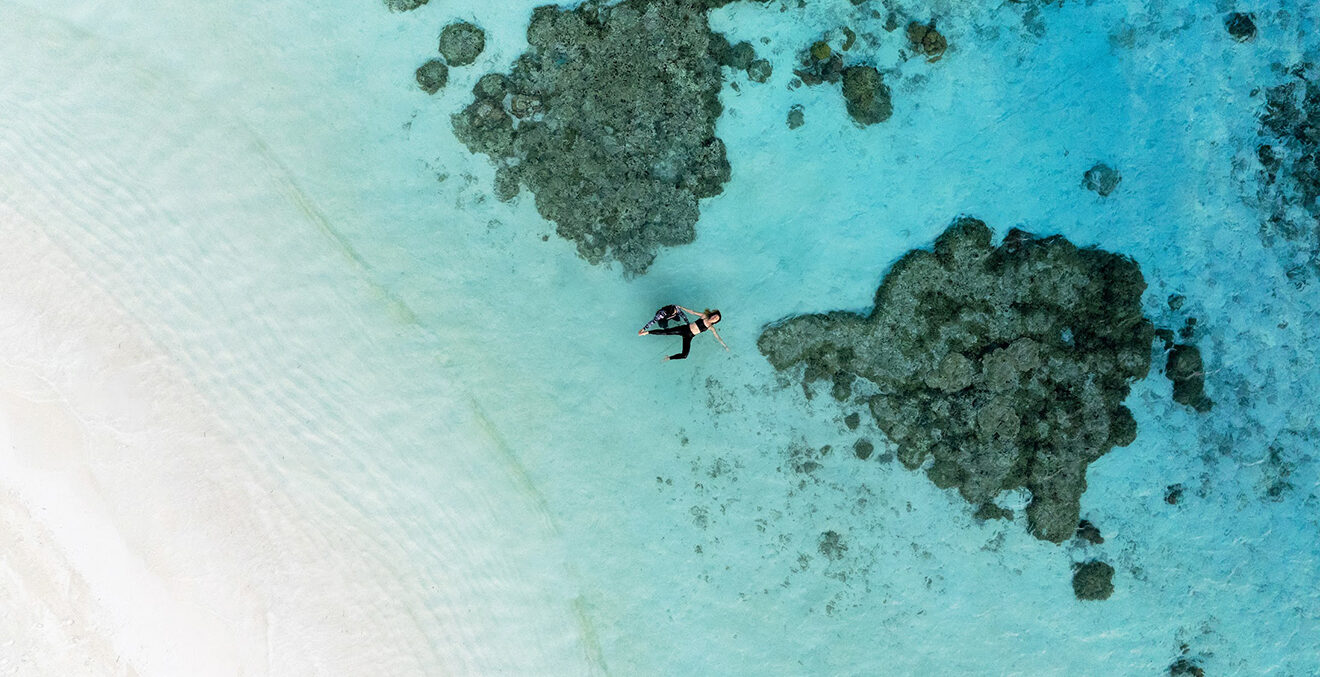 Vogelperspektive auf Strand, Meer und Felsen im Wasser.