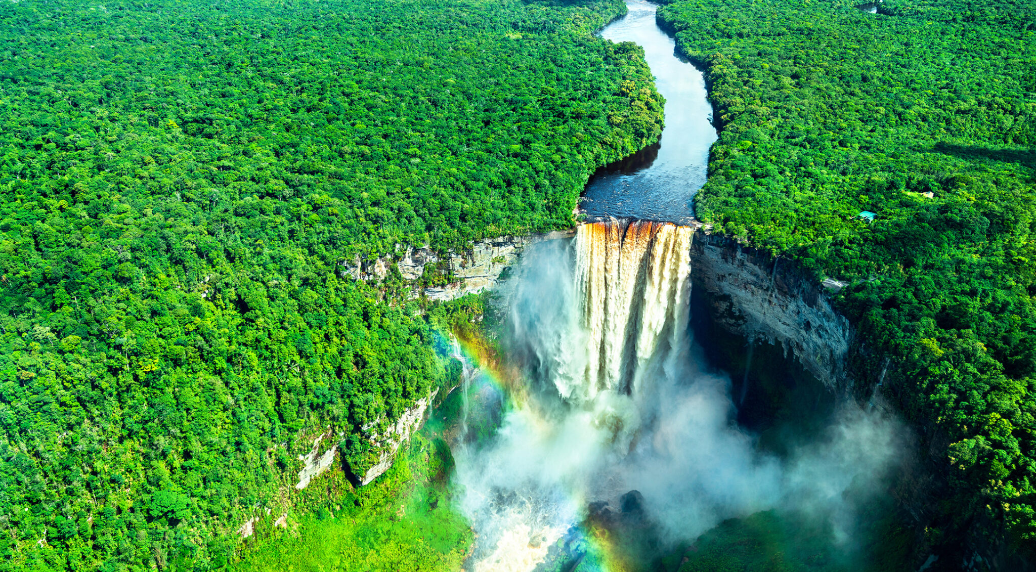 Breiter Wasserfall inmitten dichter grüner Regenwaldlandschaft, der in ein rundes Becken stürzt.