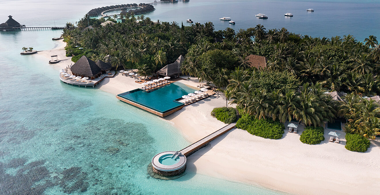 Blick von oben auf eine Insel mit Poolanlge und Bäumen.
