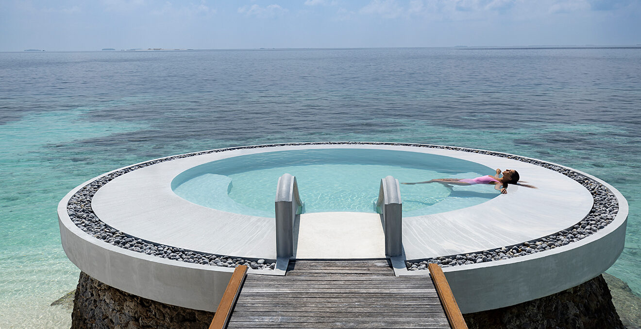 Runder Pool mit Steg, der ins Meer ragt.