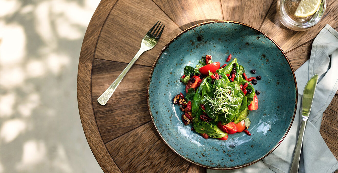 Blauer Teller mit grünem und roten Essen auf einem Holztisch.