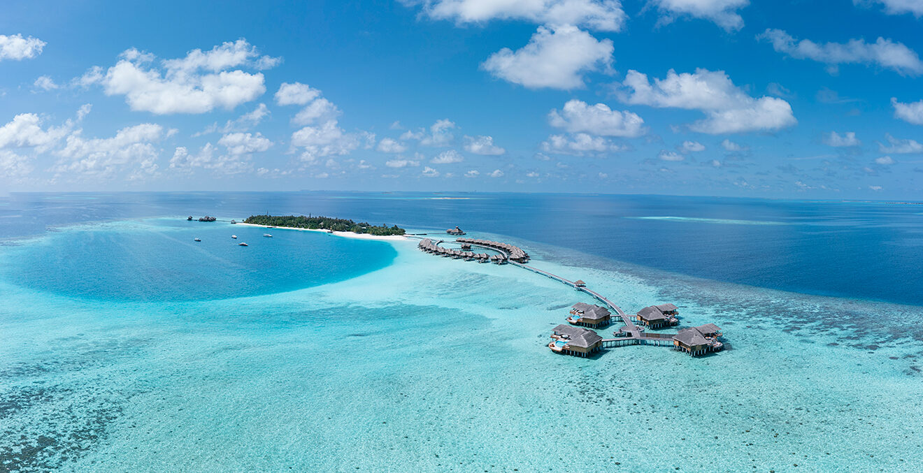 Blick auf klares, blaues Wasser mit einer kleinen Insel und Holzbauten.