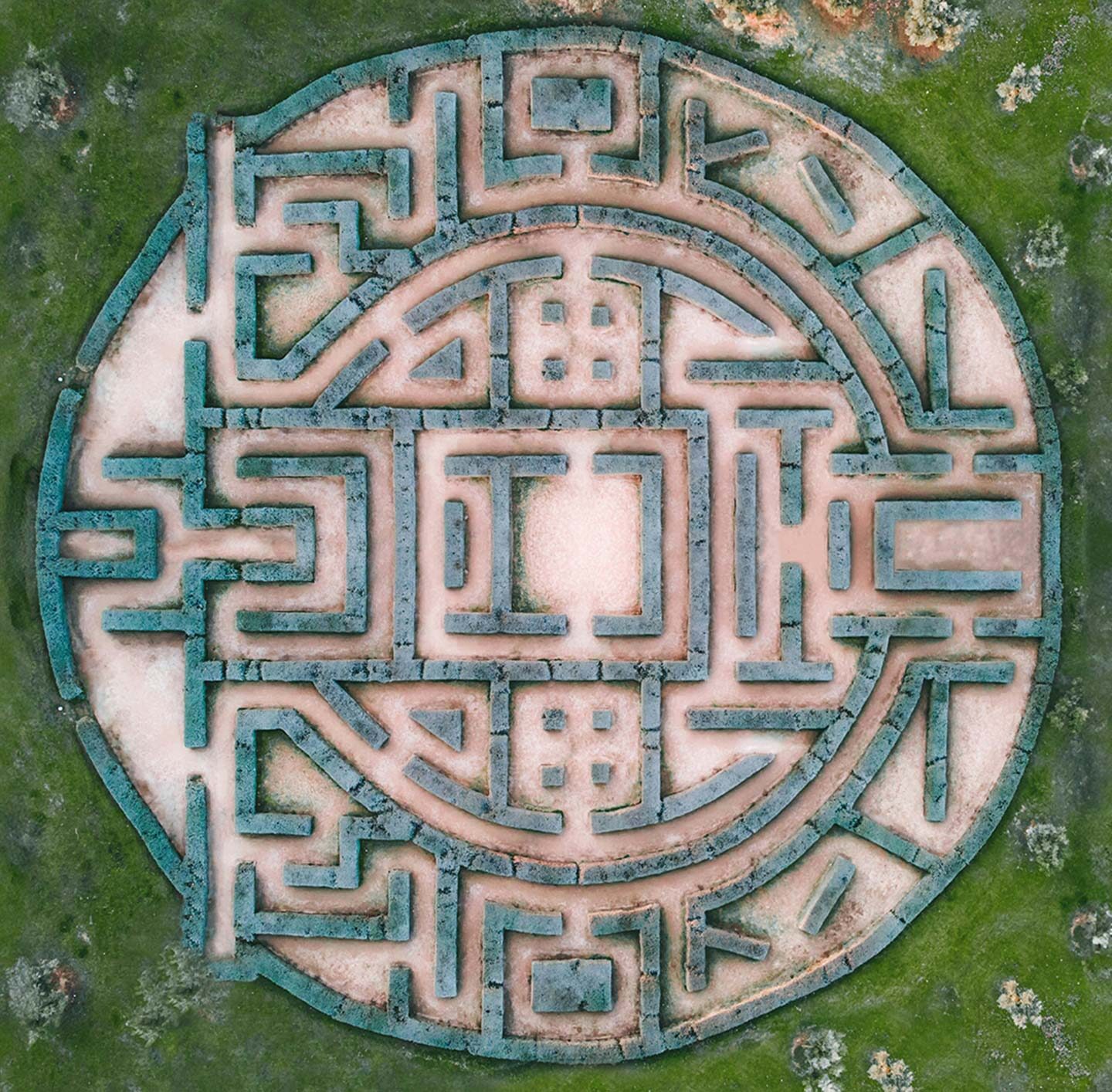 Die Aufnahme zeigt ein kreisförmiges Areal mit geometrischen Wegen und Strukturen, die an ein Mandala oder Labyrinth erinnern. Die umliegenden Bereiche sind grün bewachsen. Das Bild vermittelt eine Verbindung zwischen Struktur, Orientierung und Natur.