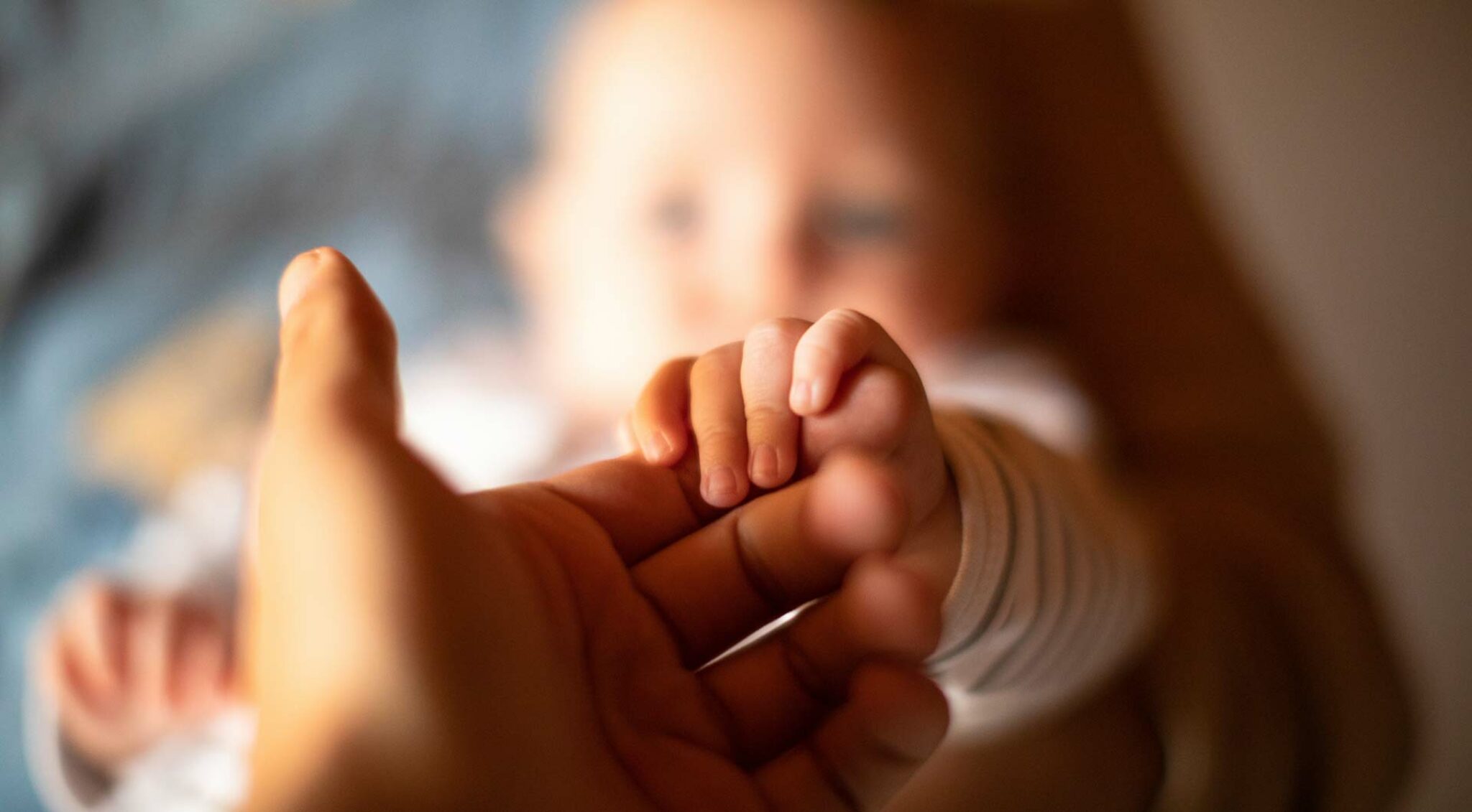 Ein Baby greift mit seiner Hand den Finger eines Erwachsenen – Symbol für Vertrauen, Fürsorge und Weitergabe von Werten.