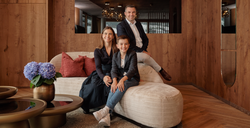 Familie Hettegger sitzt entspannt auf einem Sofa in einem gemütlichen, holzvertäfelten Raum.