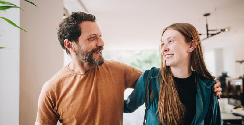Vater und Tochter haben je einen Arm um den anderen gelegt und lachen sich an.
