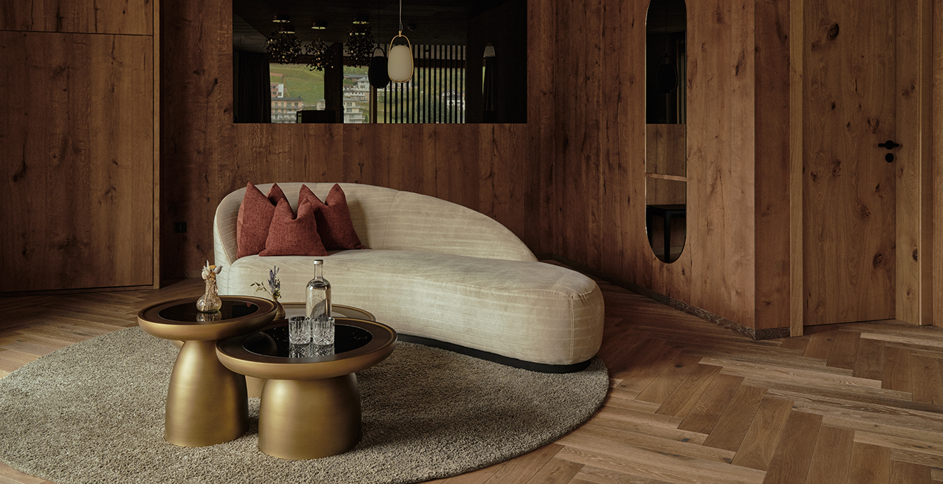 Chaiselongue mit goldfarbenen Beistelltischen vor Holzwand.