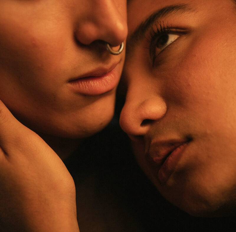 Nahaufnahme zweier aneinander geschmiegter Gesichter: Mann mit Nasenring und Frau mit dunklen Augen.