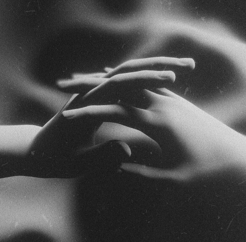 Zwei Hände greifen vor verschwommenem Hintergrund ineinander. Schwarz-weiss Aufnahme.