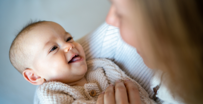 Eine Frau blickt ein lachendes Baby an, das sie in ihrem Arm hält.