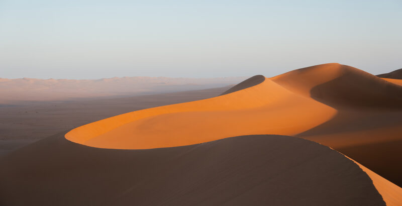 Sanft geschwungene Sanddünen mit langen Schatten bei tief stehender Sonne.