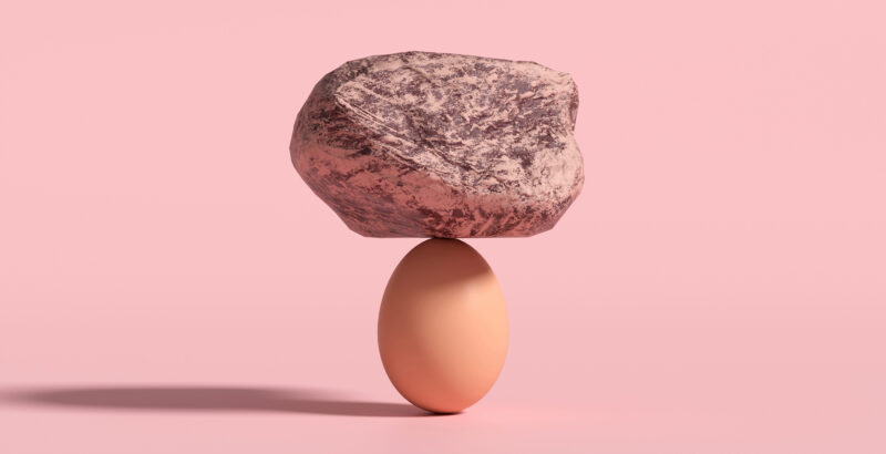 Flacher Stein, der auf einem Ei balanciert, vor rosafarbenem Hintergrund.“