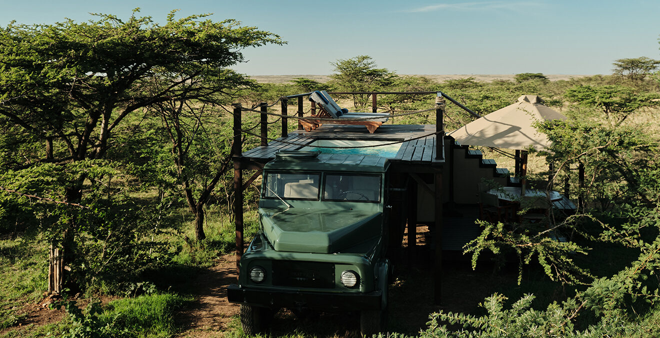 Ein alter grüner LKW steht zwischen Bäumen vor einem Zelt.