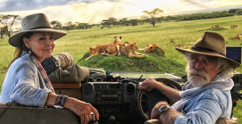 Beverly und Derek Joubert sitzen in einem offenen Safari-Fahrzeug und blicken über die Landschaft.
