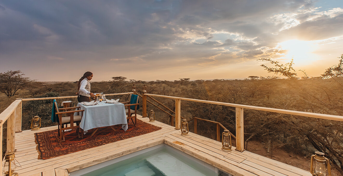 Blick von der Terrasse mit einem Tisch und weißer Tischdecke samt Swimmingpool über die Landschaft Afrikas.