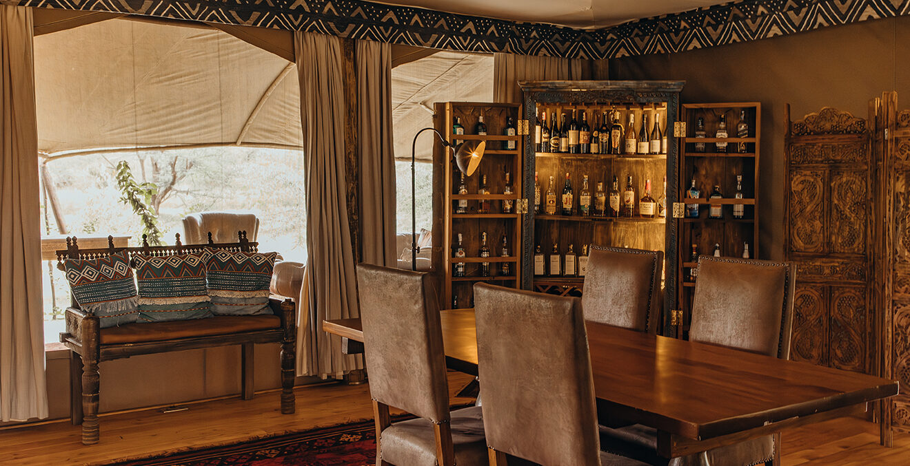 Innenbereich ders GreatPlainsConservation-MaraExpeditionCamps mit Tischen, Stühlen und einem Barschrank.