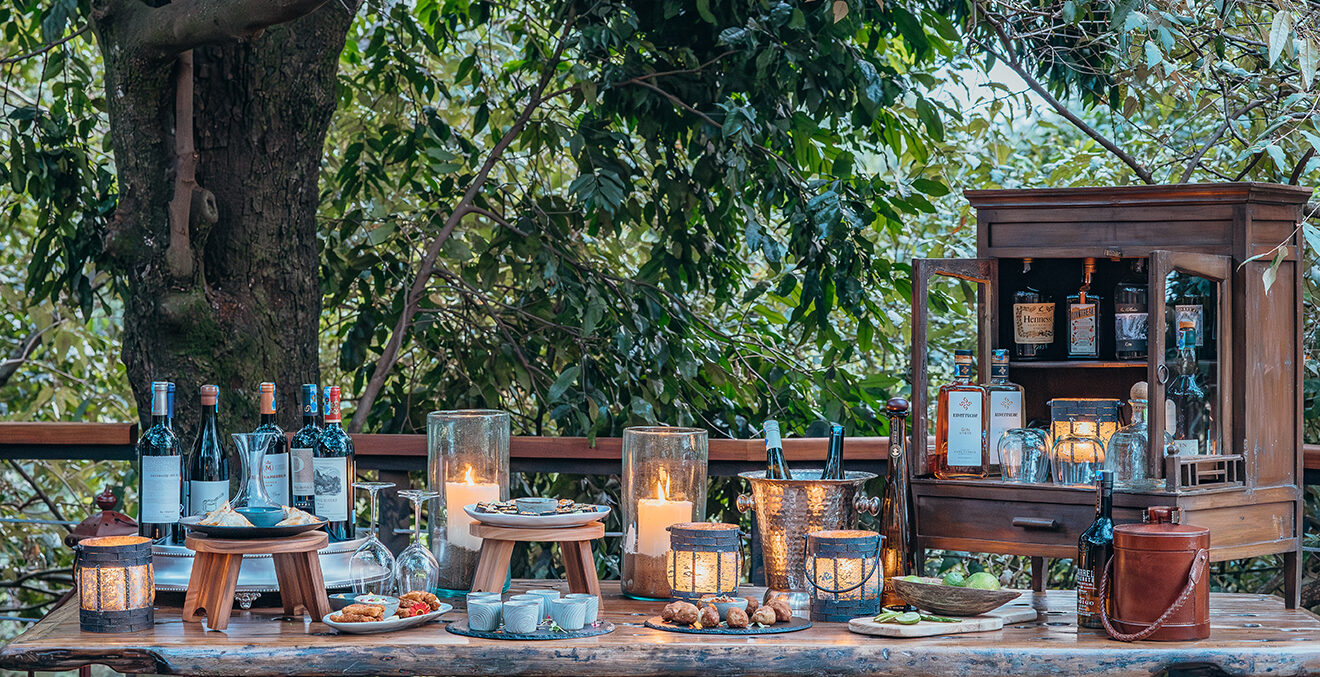 Gedeckter Tisch mit Speisen, Wein und Kerzen im Freien unter einem Baum.