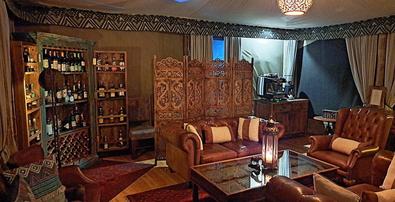 Innenbereich des Mara-Expedition-Camps mit Sofas, Tisch und Stühlen sowie einem Barschrank.