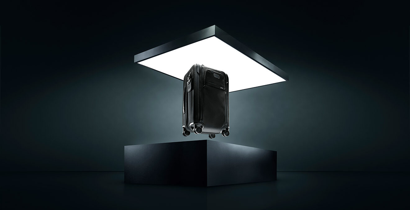 Schwarzer Koffer steht allein auf einem beleuchteten Podest in einem dunklen, futuristisch wirkenden Raum.