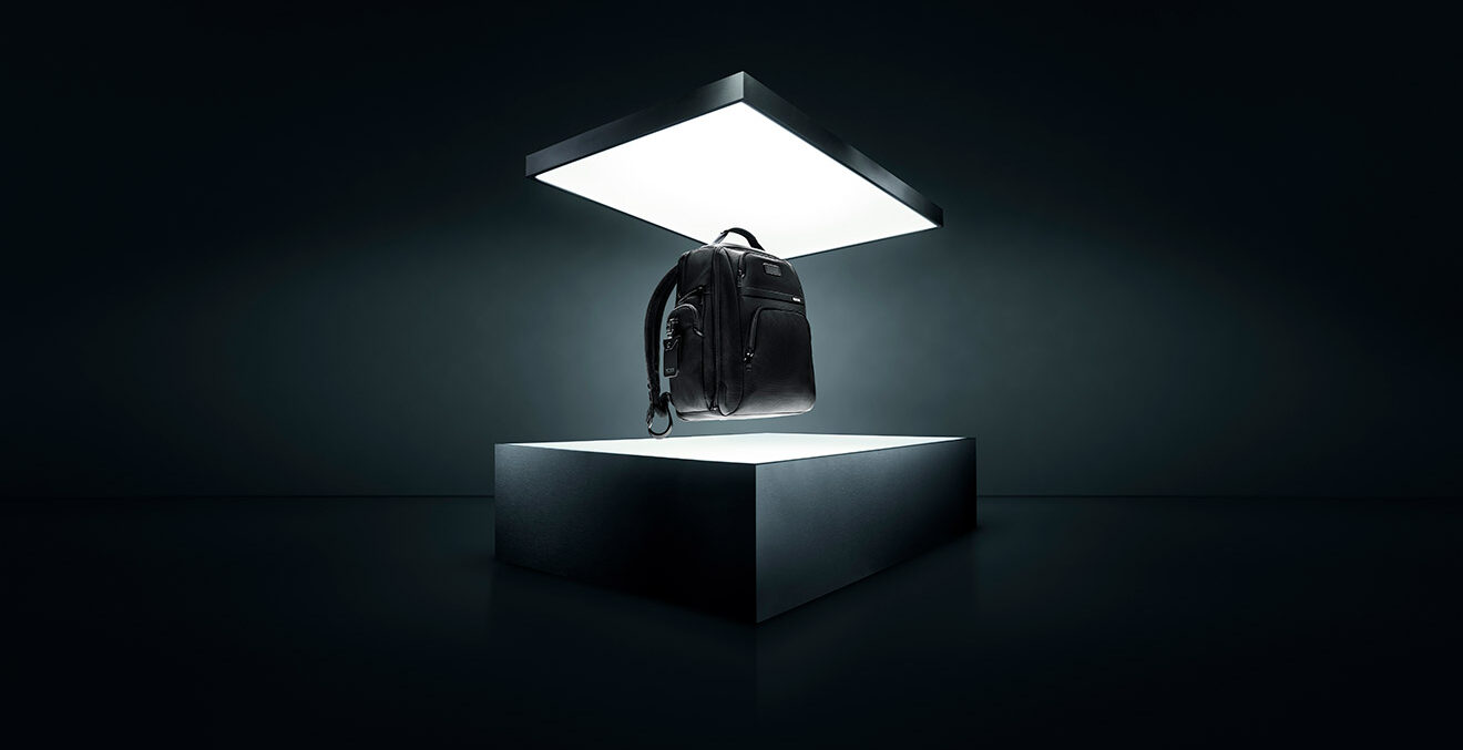 Schwarze Reisetasche steht allein auf einem beleuchteten Podest in einem dunklen, futuristisch wirkenden Raum.