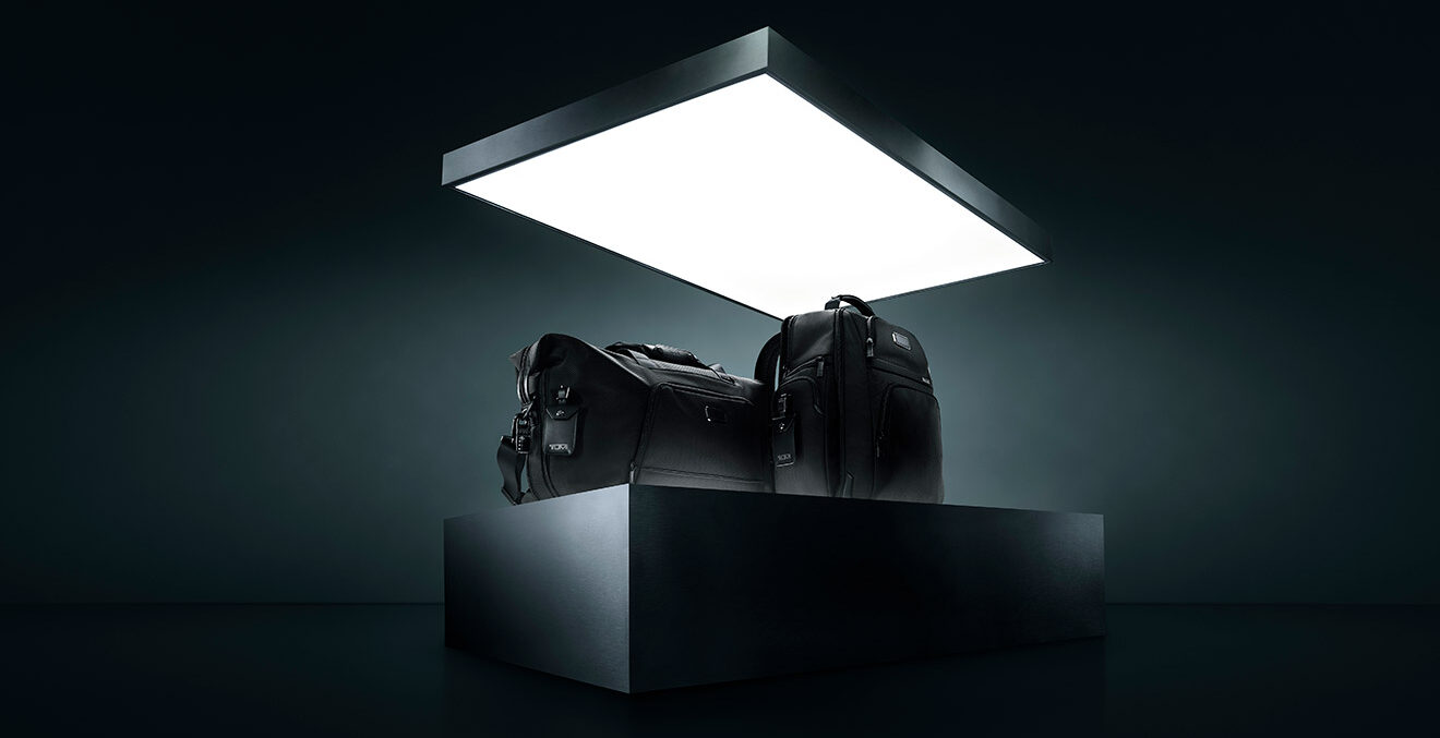 Zwei Reisetaschen stehen allein auf einem beleuchteten Podest in einem dunklen, futuristisch wirkenden Raum.