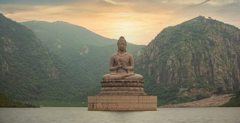 Große Buddhafigur sitzt vor einer weiten Berglandschaft mit Tal und Hügeln.