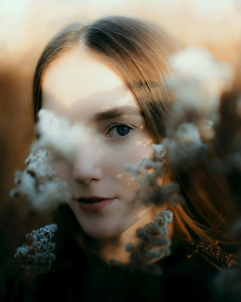 Porträt einer Frau, teilweise verdeckt durch unscharfe Pflanzen im Vordergrund.