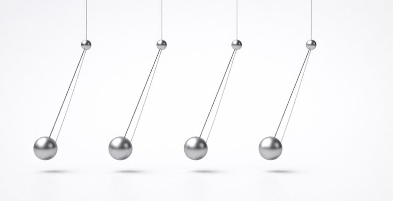Reihe von fünf Metallkugeln eines Newton-Pendels, die an dünnen Fäden hängen; die Kugeln sind leicht versetzt dargestellt, sodass eine schwingende Bewegung sichtbar wird.