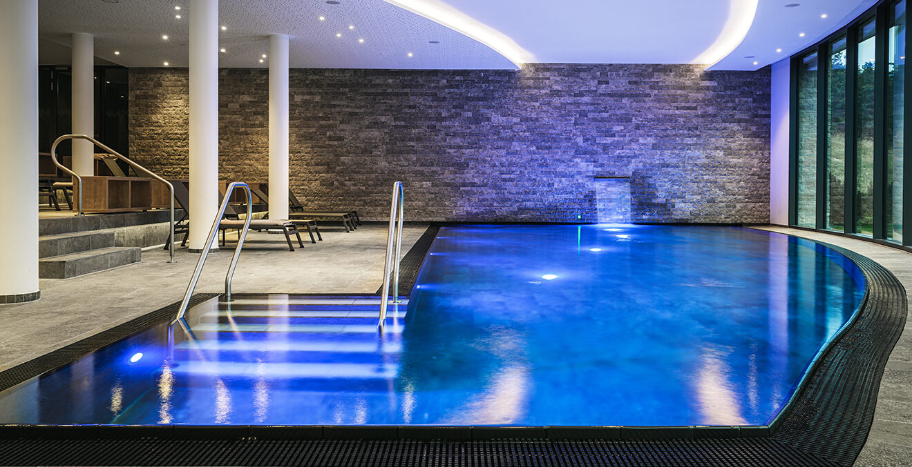Blick auf den blau-leuchtenden Indoor-Pool des AMERON-Neuschwanstein-Alpsee-Spa-&-Resort.