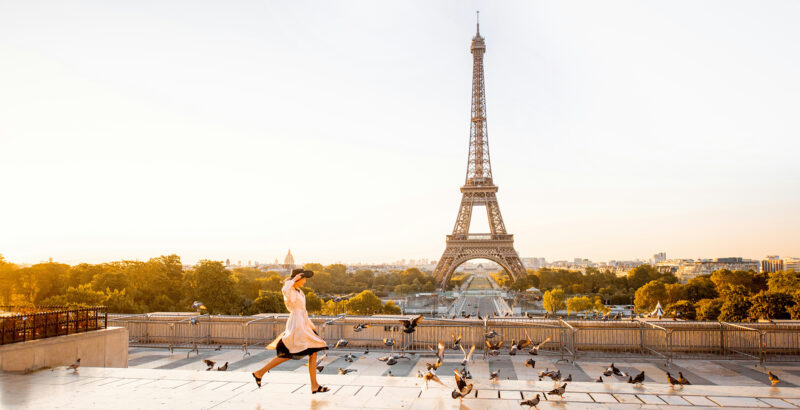 Breite Panoramaaufnahme von Paris mit dem Eiffelturm im Hintergrund; im Vordergrund läuft eine Person.