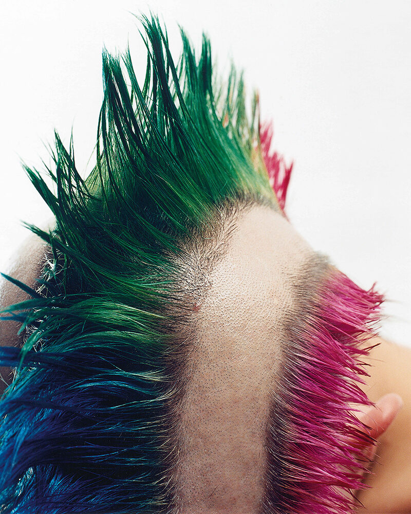 Nahaufnahme eines teilweise rasierten Kopfes mit buntem Irokesenschnitt in Grün-, Blau- und Pinktönen. Foto von Herlinde Koelbl, Projekt Haare, Punk, 2007 Fotografie, 100 x 80 cm © Herlinde Koelbl.