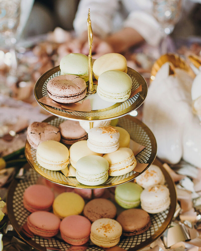 Mehrstöckige Etagere mit bunten Macarons in verschiedenen Farben wie Rosa, Gelb und Braun vor unscharfem Hintergrund.