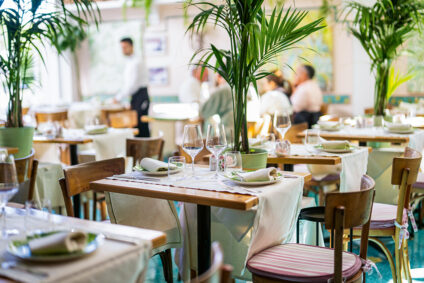 Heller Restaurantinnenraum mit Pflanzen und Holzmöbeln.