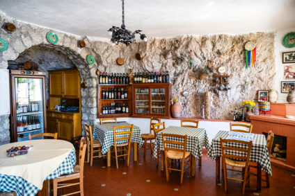 Offener Restaurantbereich mit vielen Holztischen samt karierten Tischdecken und Stühlen unter heller Decke.