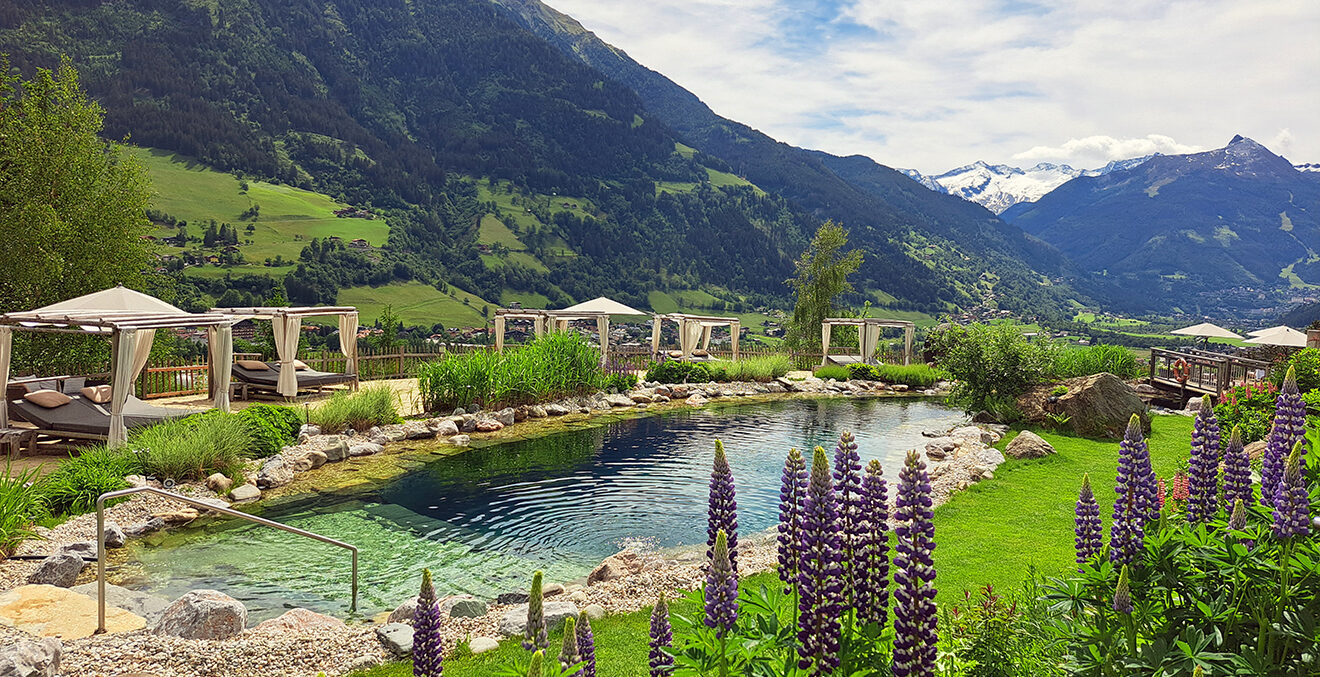 Naturpool eingebettet in grüne Wiesen mit Liegen unter Baldachinen.