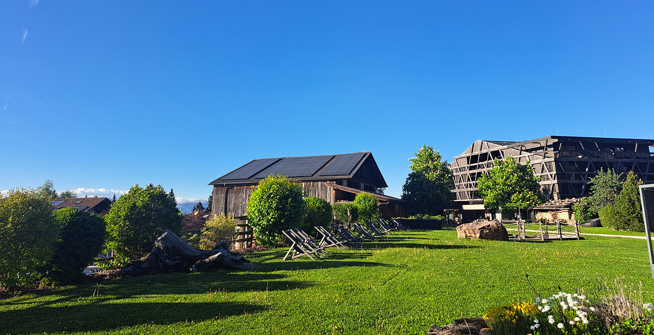 Blick über grüne Wiesen und blauen Himmel auf das Mountainhideaway Pfoesl.