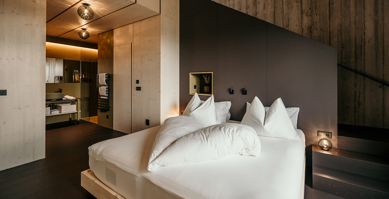 Modernes Gästezimmer im Hotel Pfoesl mit weissen Betten, Holzvertäfelung und gedeckten Farben.