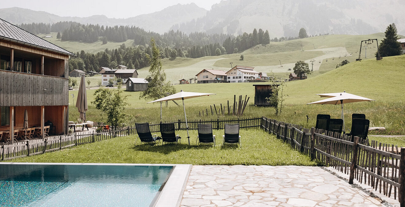 Der Außenbereich der FUCHSEGG ECO LODGE mit Pool, Liegewiese und Alpenblick.