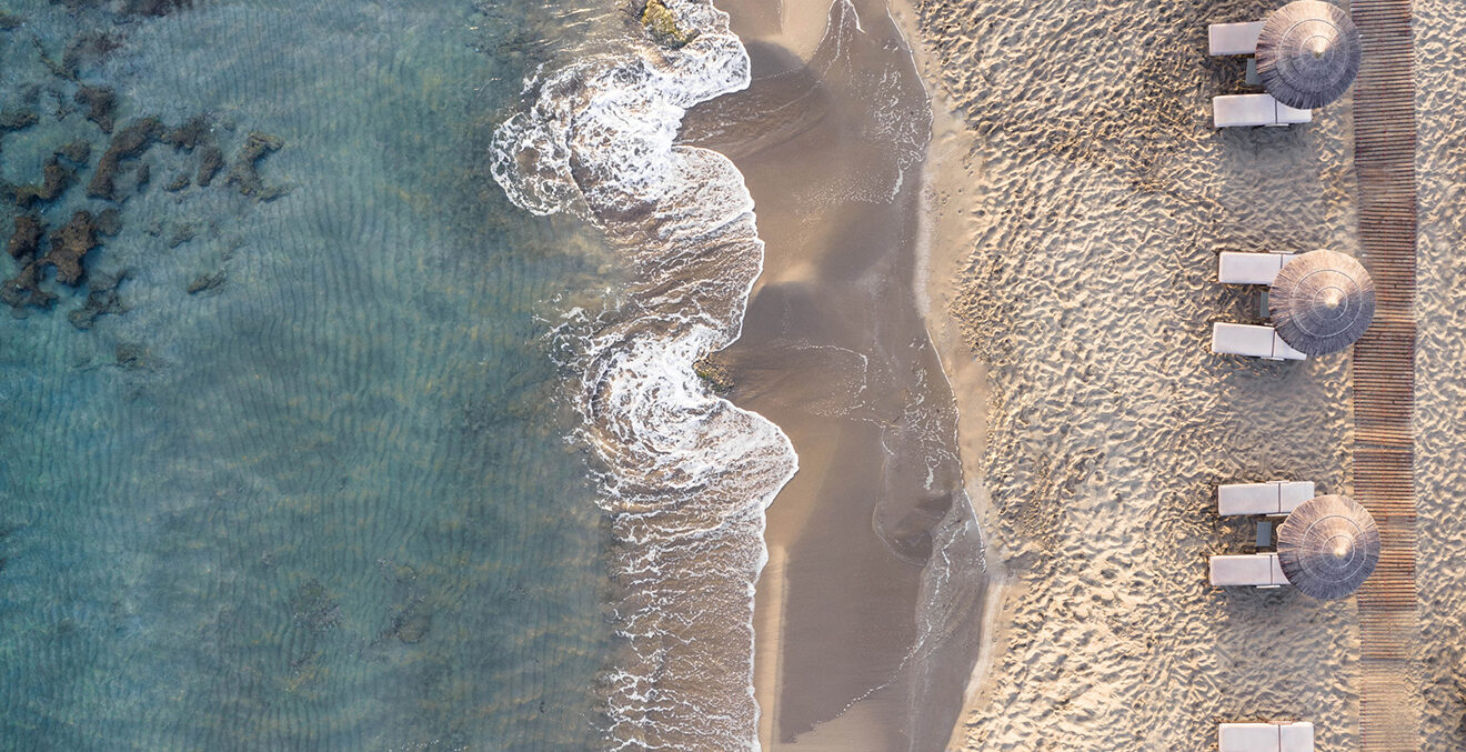 Blick von oben auf den Strand mit Liegen und Sonnenschirmen.
