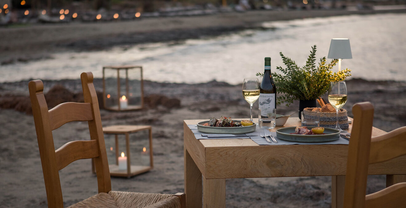 Gedeckter Tisch in der Dämmerung am Strand mit Kerzenlicht.