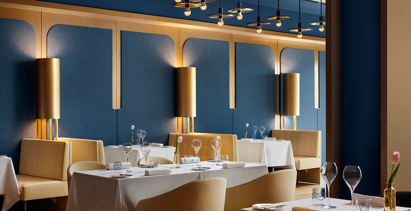 Restaurant mit dunkelblauen Wänden, weiß eingedeckten Tischen und hellbeigen Möbeln.