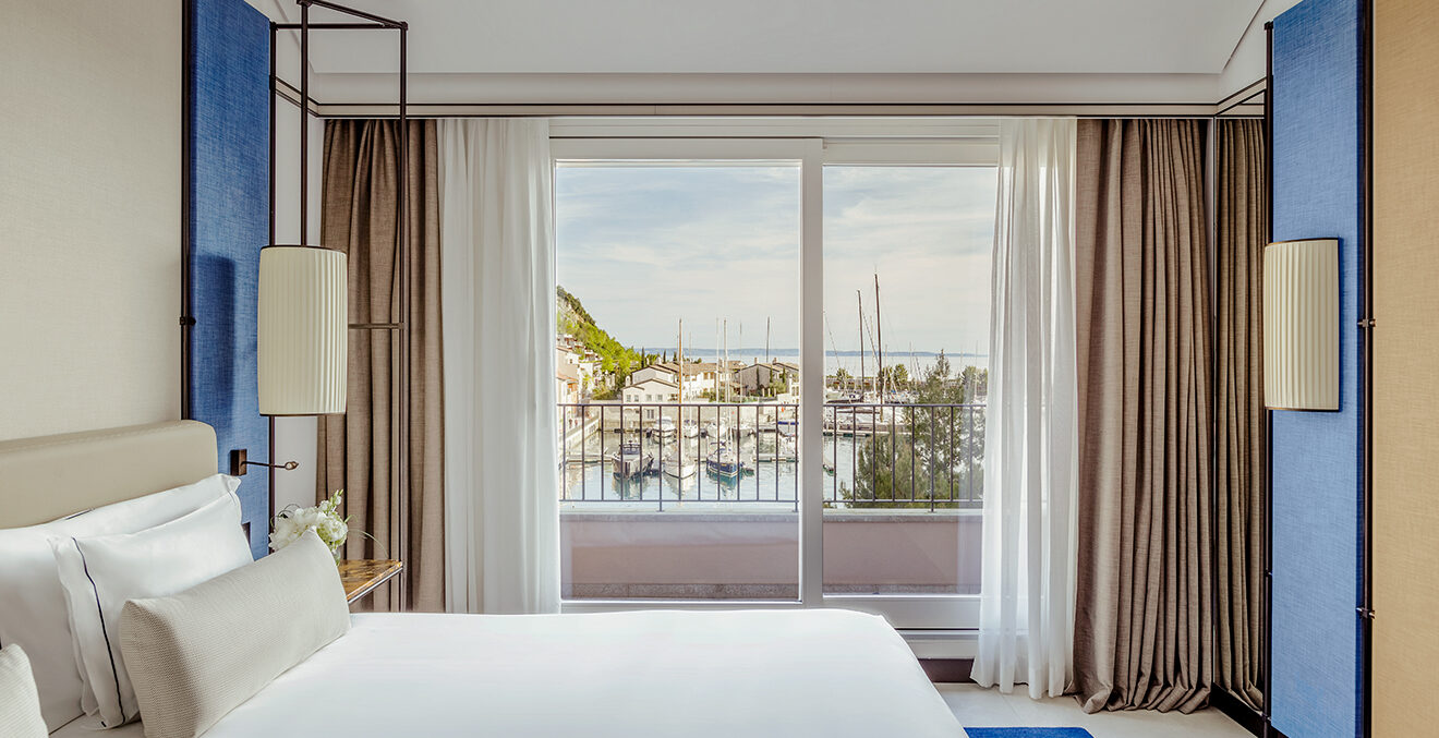 Großes Bett mit weißer Bettwäsche vor einem Panoramafenster.