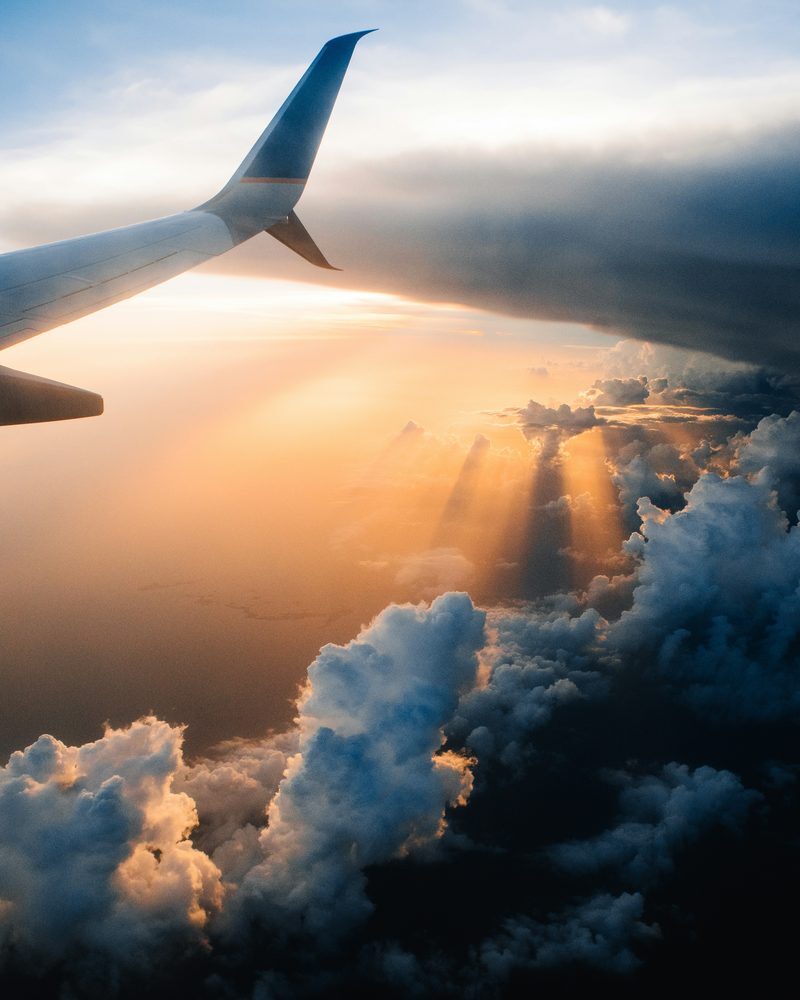 Blick aus einem Flugzeugfenster auf Tragfläche und Wolken im Sonnenuntergang