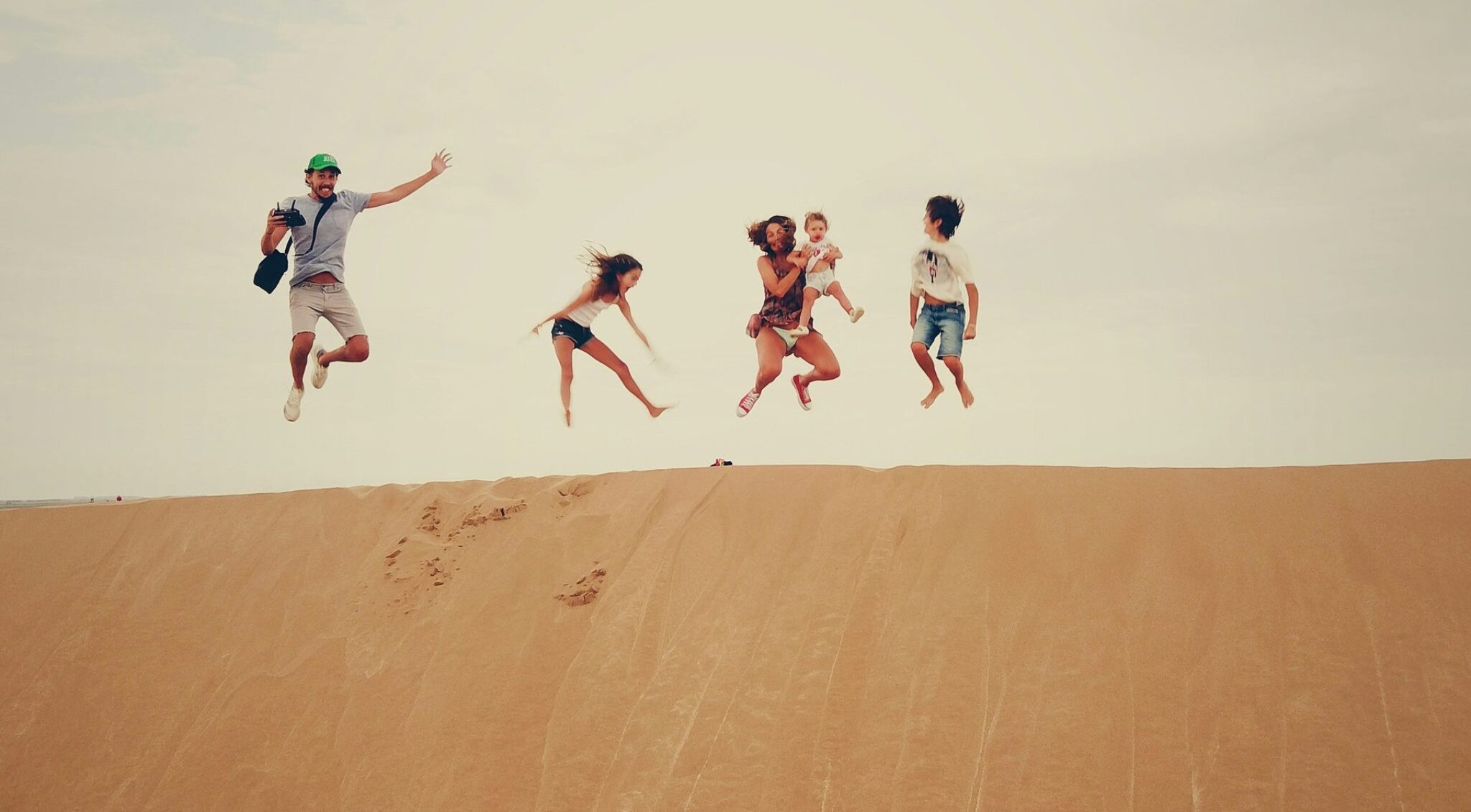 Familie springt gemeinsam auf einer Sanddüne während einer Reise